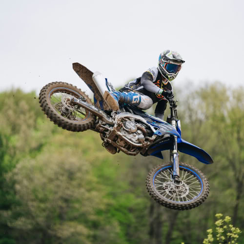 Un motocycliste effectue un saut en motocross dans un environnement boisé.