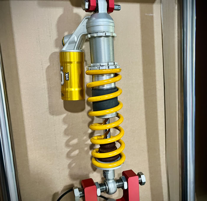 Un dispositif mécanique avec un ressort hélicoïdal orange à l'intérieur d'un cadre métallique rectangulaire.