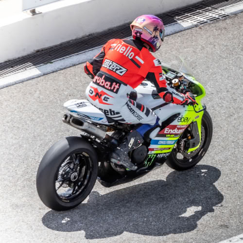 Motard en combinaison rouge et casque rose sur une moto de course.